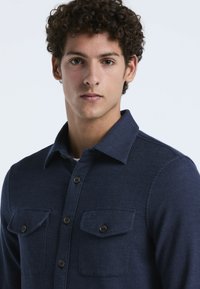 Navyblauwe button-up shirt van textuurstof met een kraag, twee borstzakken en bruine knopen voor sluiting.