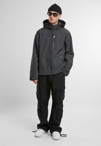 Fekete párnázott dzseki kapucnival, cipzárral és oldalsó zsebekkel. Laább van egy laza illeszkedésű fekete cargo nadrág, amely több zsebbel rendelkezik. Fehér sportcipők.