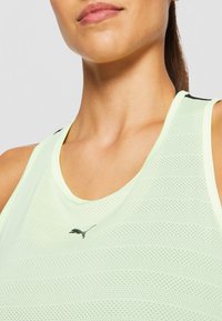 Jasnozielony siatkowy sportowy top na ramiączkach z okrągłym dekoltem i czarnym logo Pumy na środku, z oddychającą strukturą i fasonem z wycięciem na plecach.