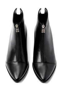 Para czarnych skórzanych botków za kostkę z przednimi suwakami i spiczastymi noskami, sfotografowanych z góry na białym tle.