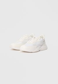 Pair of white low-top sneakers with lace-up front and thick soles, positioned side by side on a plain light background.