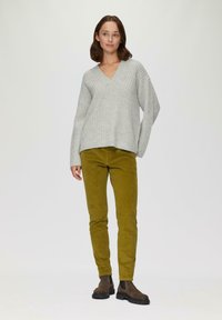 Lichtgrijze gebreide trui met een V-hals, gecombineerd met mosterdgele corduroy broek en bruine enkelboots. Eenvoudig ontwerp en relaxte pasvorm.