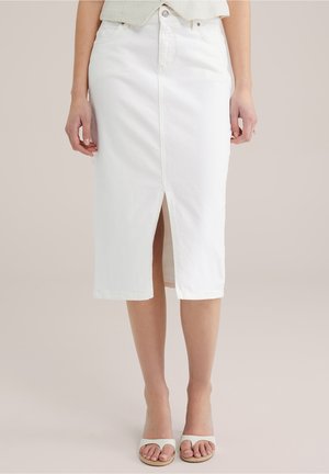 Vrouw draagt een witte denim midi-rok met een voorste split, gecombineerd met witte slidesandalen op een neutrale achtergrond.