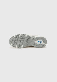 Baskets blanches avec une semelle grise texturée. Présente un motif de semelle avec des accents bleus près du talon. Design léger pour un confort optimal.