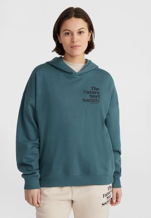 Turkusowa hoodie o luźnym kroju i regulowanym sznurku. Posiada grafikę na klatce piersiowej, prążkowane mankiety i dół. W zestawie z jasnymi spodniami.