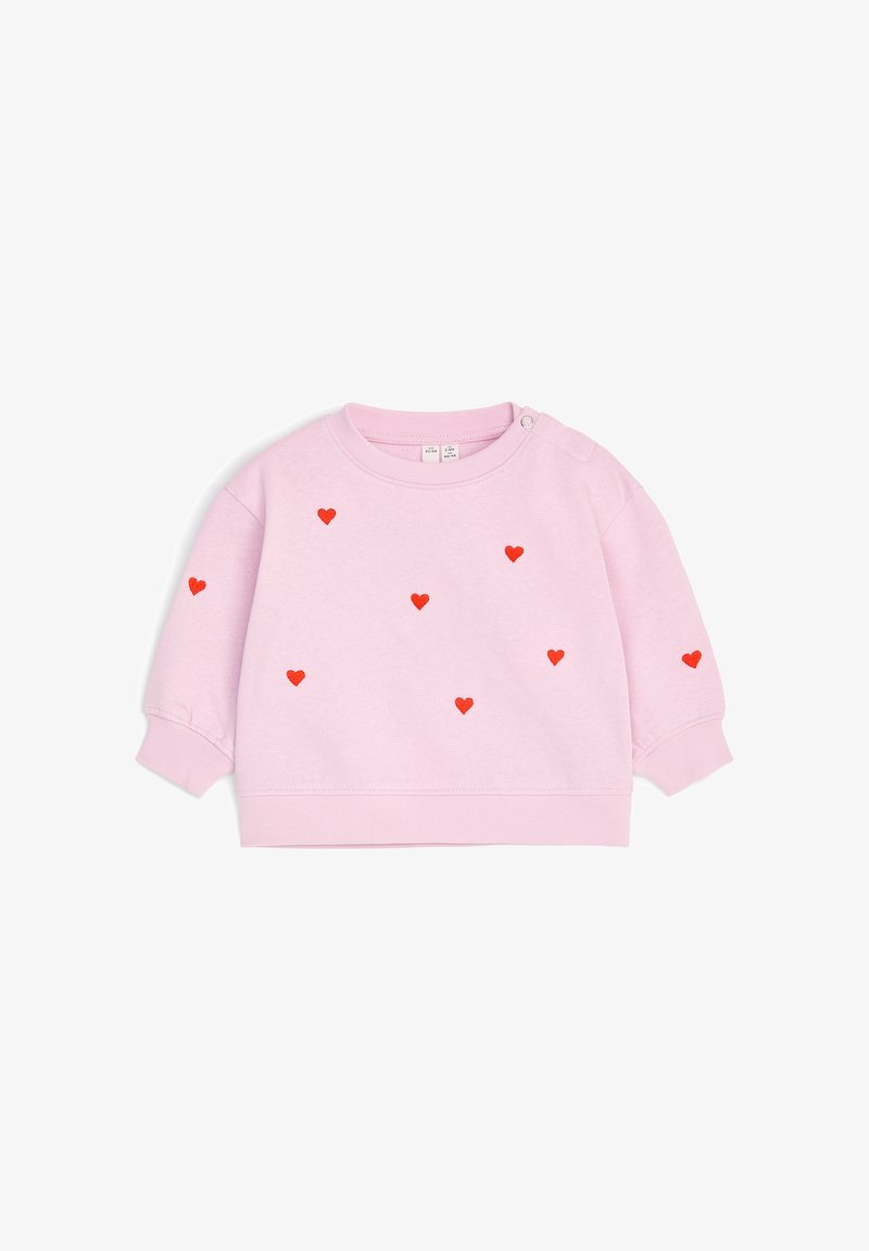 Sweat-shirt bébé à manches longues rose clair avec petits motifs de cœurs rouges dispersés sur le devant et les manches, avec boutons-pression sur une épaule.