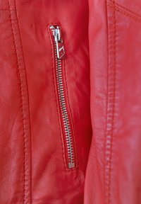 Rote Lederjacke mit einer silbernen Reißverschlusstasche, glatter Textur und Steppnähten entlang der Nähte.