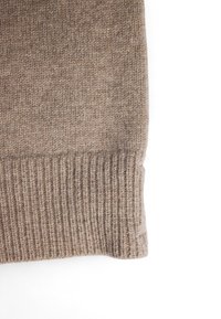 Rjava pletiva srajce, ki ima rebrast manšeto z mehko teksturo in subtilnimi odtenki, ki poudarjajo toploto tkanine.