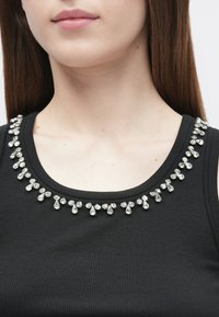 Fekete bordázott ujjatlan felső kerek nyakkivágással, amelynek szélét különböző csepp alakú, átlátszó kristálydíszek díszítik.