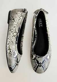Čiernobiele baleríny s hadím vzorom, zaoblenou špičkou a malou mašličkou na päte. Hladký syntetický materiál s textúrovaným vzorom.
