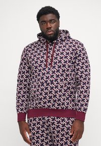 Bordeaux og marineblå mønstrede hoodie med snor i hætten, ribbede manchetter og bund. Har et geometrisk design med kontrasterende accenter.