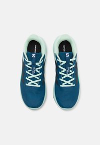 Baskets de sport bleues avec une tige en maille, accents bleu marine et vert menthe, lacets blancs et un logo sur la languette. Design moderne pour la course.