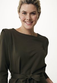 Mörkgrön klänning med långa ärmar, bred halsringning och knytning i midjan. Slätt tyg med en lätt lyster, med mjukt draperade axeldetaljer.