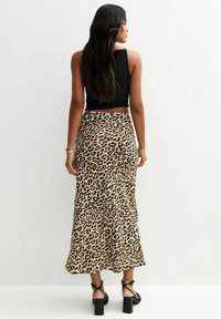 Leopard print midi skirt in beige and black fabric, with a flowing design and subtle sheen, paired with a black cropped top and strappy heels.