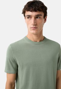 Groene gebreide t-shirt met een ronde halslijn en korte mouwen, met een gestructureerde afwerking en omgevouwen mouw cuffs.