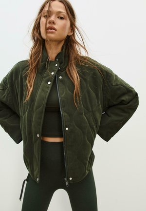 Quilted grüne Bomberjacke mit hohem Kragen, Druckknöpfen und Reißverschluss. Weicher Stoff mit einem strukturierten Muster, kombiniert mit passenden Leggings.