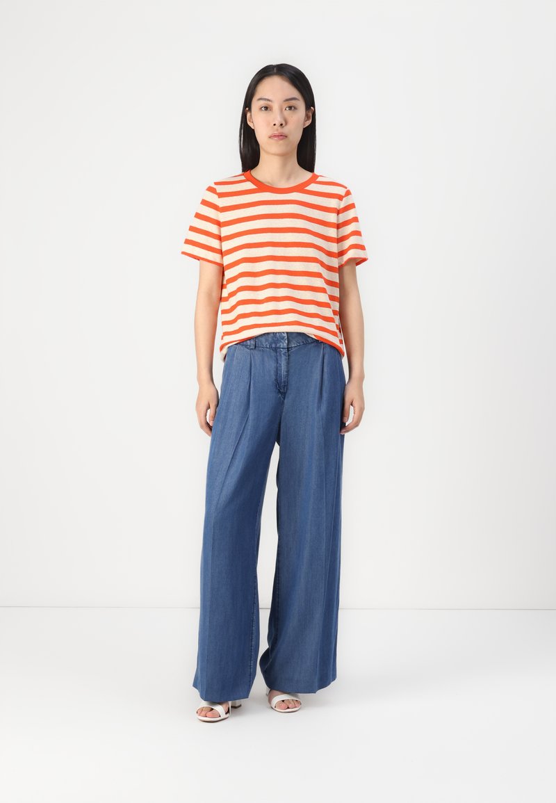 Gestreiftes orange-beige T-Shirt kombiniert mit weit geschnittenen Jeanshosen. Lässiger Schnitt, kurze Ärmel, leichtes Material, Vorderfalten-Detail an der Hose.