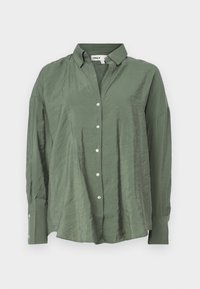 Chemise verte à col, manches longues et coupe décontractée. Le tissu semble léger avec une texture légèrement froissée.