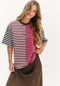 Koszulka w paski w różnych kolorach, w tym różowym, brązowym, pomarańczowym i czarnym, z haftem motyla z przodu.