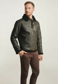 Czarna skórzana kurtka o teksturowej powierzchni, z futrzanym kołnierzem, zamek z przodu i boczne kieszenie. Połączona z brązowymi spodniami.