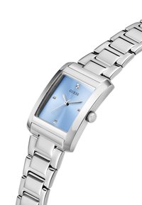 Montre rectangulaire argentée avec un cadran bleu clair, quatre index horaires argentés et un petit diamant. Équipée d'un bracelet en maillons métalliques argentés.
