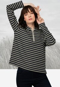 Camicia a righe blu navy e crema a maniche lunghe con una zip a metà e colletto; vestibilità comoda e tessuto morbido; indossata con jeans scuri.