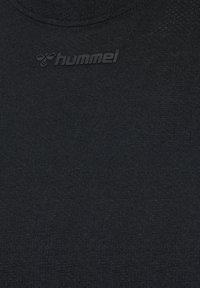 Schwarzer Stoff mit dezent eingeprägtem Hummel-Logo und Bienen-Emblem nahe dem runden Halsausschnitt.