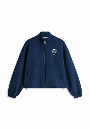 Chaqueta azul marino con cremallera, puños elásticos, dos bolsillos delanteros y logo blanco de Tommy Hilfiger en el pecho izquierdo.