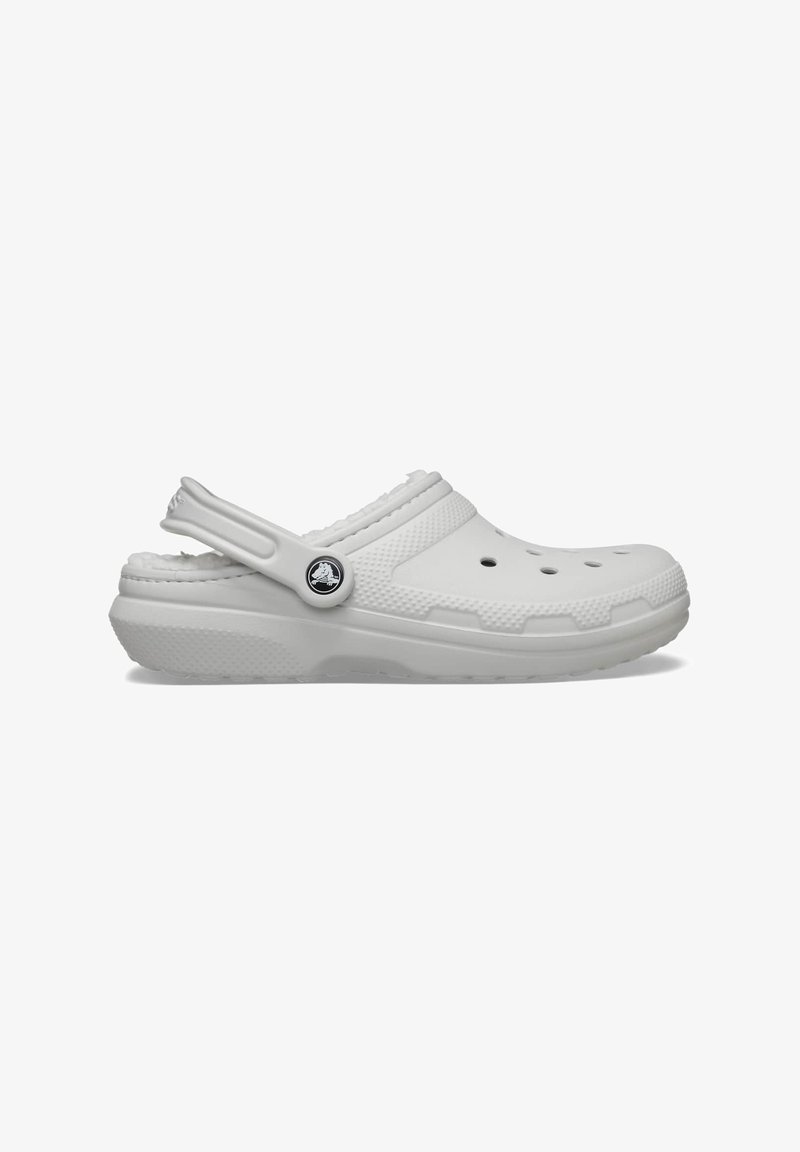 White clogs with ventilation holes and a textured strap. Features a soft lining, molded design, and a round logo accent on the side.