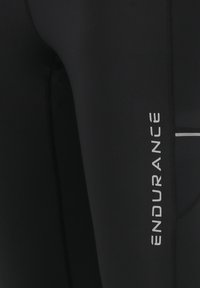 Mustat urheilulegginsit, joissa on tyylikäs muotoilu, teksturoitu kangas ja hopeinen "ENDURANCE"-logo sivussa. Slim fit ja vähäiset saumat.