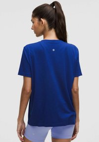 Blaues kurzärmliges T-Shirt aus weichem Stoff, mit Rundhalsausschnitt und einem kleinen Logo-Detail nahe des oberen Rückens. Minimalistisches Design.