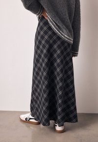 Jupe longue à carreaux noirs et gris fabriquée dans un tissu à la texture lisse, associée à des baskets blanches avec des accents noirs et des semelles marron.