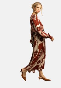 Lång klänning i röd och krämfärgad tyg med blommönster, bjällraärmar och volang i fållen. Bärs med bruna klackskor. Slät textur.