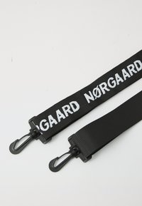 Schwarzer verstellbarer Gurt mit weißem "NØRGAARD"-Text. Enthält robuste schwarze Metallclips an beiden Enden zur Befestigung. Flach gewebte Textur.