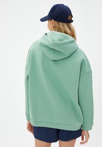 Sudadera con capucha de color verde claro, de corte holgado, con una gran capucha y puños acanalados, combinada con pantalones cortos azul marino. Textura suave.