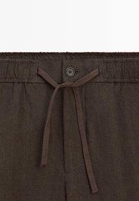 Pantalon en lin marron avec une ceinture élastique, un bouton à l'avant et un cordon noué au centre.