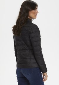 Svart puffjacka med kviltad design, hög krage och långa ärmar. Lätt material, figursydd form och slät textur.