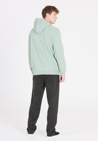 Lichtgroene hoodie met een trekkoord in de capuchon en geribbelde manchetten, gecombineerd met donkergrijze sweatpants. Glad materiaal, relaxte pasvorm en minimale details.