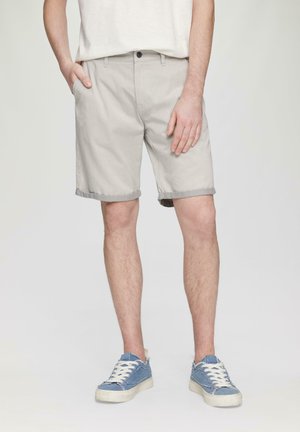 Shorts en coton gris clair avec des revers, poches avant et fermeture à un bouton. Assortis à des baskets en denim bleu.