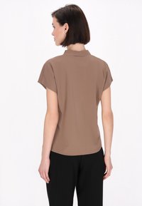 Blusa marrone a maniche corte con un delicato lucido, dotata di colletto alla cinese e vestibilità comoda, abbinata a pantaloni neri.