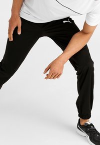 Svarta träningbyxor med elastiska mudd, med en vit Puma-logotyp. Byxorna har en slät yta och en slim fit-design.