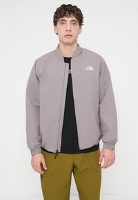 Ανοιχτό γκρι μπουφάν bomber με στρογγυλεμένη γιακά, μανίκια με μανσέτες και φερμουάρ μπροστά, με το λογότυπο North Face στο αριστερό στήθος.