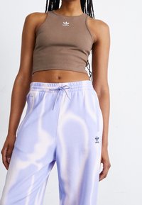 Brun ribbad crop top med vit Adidas-logga, kombinerad med ljuslila sweatpants med mönster i tie-dye och svart Adidas-logga vid höfterna.