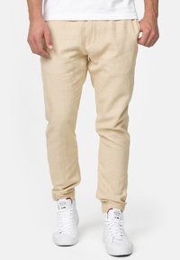 Pantalones jogger de lino beige con un ajuste tapered, cintura elástica y bolsillos laterales, combinados con zapatillas altas blancas.