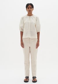 Blusa crema a maniche a palloncino, morbida, con scollo a chiave; abbinata a pantaloni beige sartoriali e sandali neri. Texture lisce in tutto il look.