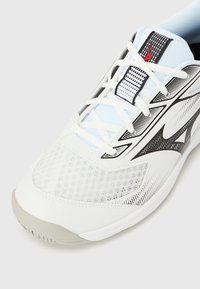 Λευκό αθλητικό παπούτσι με πλεκτό επάνω μέρος, μαύρες λεπτομέρειες και υφή στη σόλα. Διαθέτει κλείσιμο με κορδόνια και χαρακτηριστικά μοτίβα στα πλάγια.