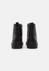 Botas de tobillo de cuero negro con una textura lisa, que cuentan con cremalleras laterales, tiradores y una suela de goma negra resistente.
