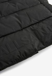 Melna polsterēta jaka ar gludu, spīdīgu audumu. Iezīmēta ar izcilu "ALLSAINTS" logo un horizontāliem kviltētiem posmiem. Minimālistisks dizains.