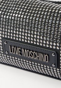 Svart väska med glänsande metallnitar, en texturerad yta och en framträdande platta med varumärket "LOVE MOSCHINO".