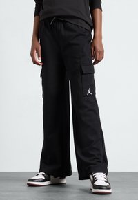 Czarne spodnie cargo z bawełny, o luźnym kroju, z bocznymi kieszeniami i białym logo Jordana na udzie. W zestawie z czarno-białymi sneakerami.